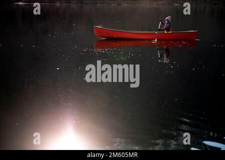 I bambini locali pagaiano in una canoa rossa in una fredda giornata invernale su un tranquillo e bellissimo lago di Bohinj nella regione di Gorenjska in Slovenia Foto Stock