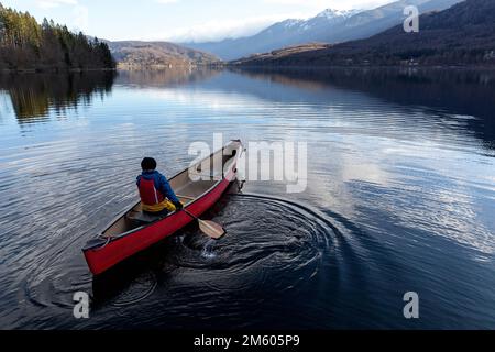 I bambini locali pagaiano in una canoa rossa in una fredda giornata invernale su un tranquillo e bellissimo lago di Bohinj nella regione di Gorenjska in Slovenia Foto Stock