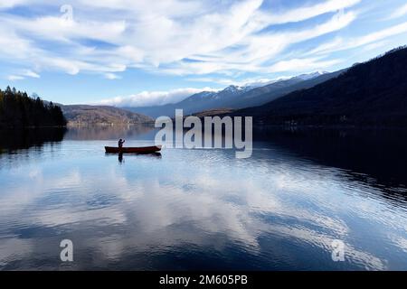 I bambini locali pagaiano in una canoa rossa in una fredda giornata invernale su un tranquillo e bellissimo lago di Bohinj nella regione di Gorenjska in Slovenia Foto Stock