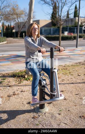 Donna che fa ginnastica su un apparato pubblico in un parco cittadino per allenarsi e rimanere in buona salute. Foto Stock