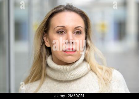 Ritratto di una bella donna bionda di mezza età in un maglione di dolcevita bianco in piedi con un look premuroso su uno sfondo bianco luminoso dentro Foto Stock