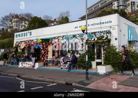 Western Esplanade, Southend on Sea, Essex, Regno Unito. 1st Jan, 2023. La gente è fuori a godersi il clima mite di Capodanno lungo il lungomare di Southend, con alcuni pasti fuori dalla gelateria Rossi con le sue colorate decorazioni natalizie Foto Stock