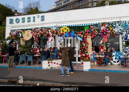 Western Esplanade, Southend on Sea, Essex, Regno Unito. 1st Jan, 2023. La gente è fuori a godersi il clima mite di Capodanno lungo il lungomare di Southend, con alcuni pasti fuori dalla gelateria Rossi con le sue colorate decorazioni natalizie Foto Stock