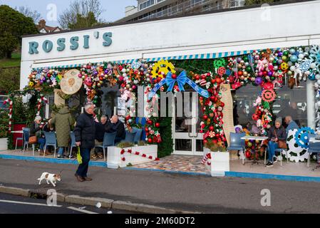 Western Esplanade, Southend on Sea, Essex, Regno Unito. 1st Jan, 2023. La gente è fuori a godersi il clima mite di Capodanno lungo il lungomare di Southend, con alcuni pasti fuori dalla gelateria Rossi con le sue colorate decorazioni natalizie Foto Stock