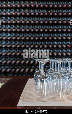 Bicchieri da vino vuoti con molte bottiglie impilate come sfondo, preparazione alla degustazione di vini nella cantina di Lanzarote, Spagna Foto Stock