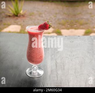 Frullato di fragola sano in vetro su legno scuro. Frullato di fragola su legno scuro con fondo sfocato. Primo piano delizioso frullato di fragole Foto Stock