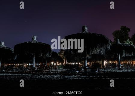 Silhouette sdraio e ombrelloni disposti sulla spiaggia sotto il cielo di notte Foto Stock