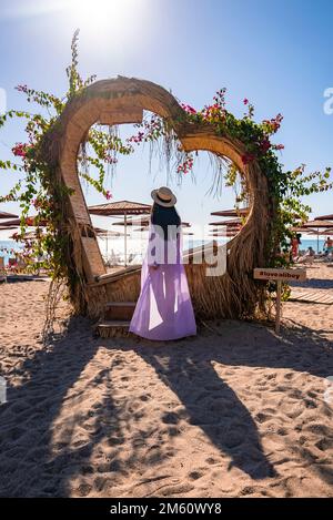 Vista posteriore della donna in piedi da una struttura a forma di cuore in spiaggia Foto Stock