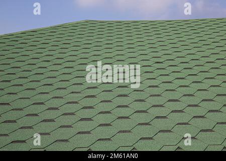 Copertura fatta di tegole verdi di bitume morbido su un tetto a fianchi di una casa. Vista ravvicinata del tetto di asfalto sfondo piastrella verde. Tegole verdi sul tetto Foto Stock