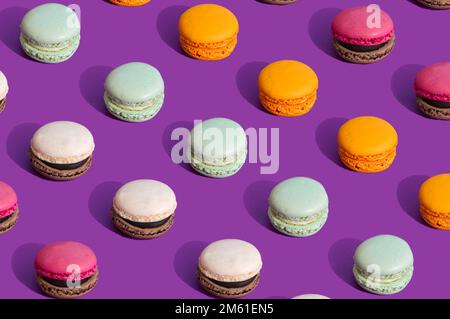 Macaron colorati su sfondo viola scuro. Modello estivo di cibo dolce. Concetto di vita morta estetica. Colori alla moda con forte contrasto. Foto Stock