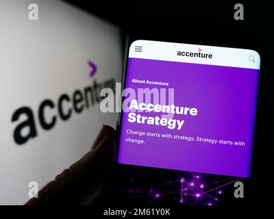 Persona che tiene il cellulare con la pagina web della società di informatica Accenture plc sullo schermo con il logo. Messa a fuoco al centro del display del telefono. Foto Stock