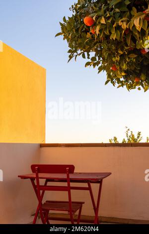 Tavolo e sedie di legno rosso sotto un albero d'arancio sulla terrazza di una casa al tramonto Foto Stock