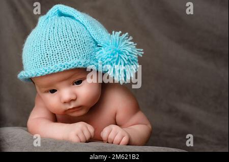 Rivne, Ucraina 25 aprile 2022: Un bambino neonato con un cappuccio blu giace sullo stomaco, ritratto da vicino. Foto Stock