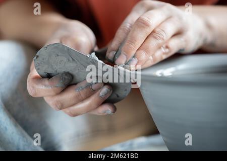 Ceramista che usa la nervatura metallica per la formatura della ceramica, vasaio che lavora con argilla su ruota Foto Stock