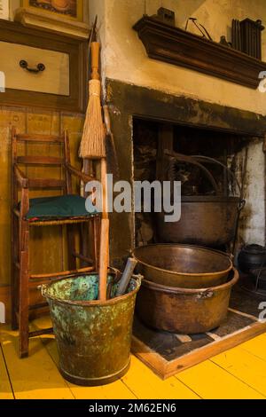 Seggiolone accanto al caminetto con pentole e bollitori antichi nella sala da pranzo all'interno di una vecchia casa di pietra di campagna canadese del 1838. Foto Stock