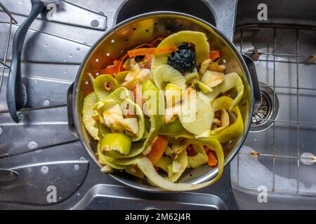 Peelings di frutta e verdura in un colander di metallo in una cucina residenziale come parte di preparazione di un pasto. Foto Stock