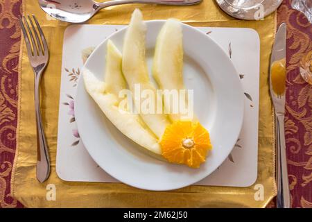 Fette di melone di melone di melone di miele guarnite con una fetta di arancia servita come antipasto in un pasto a tre portate. Foto Stock