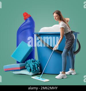 Giovane donna e grande secchio con forniture di pulizia su sfondo verde Foto Stock