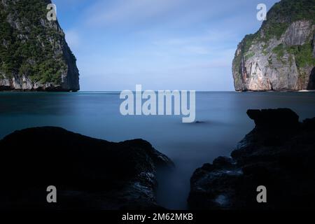 Vista dalla spiaggia Maya che si affaccia sulle scogliere rocciose. La lunga esposizione dà un mare liscio e serico. Rocce in primo piano. Foto Stock