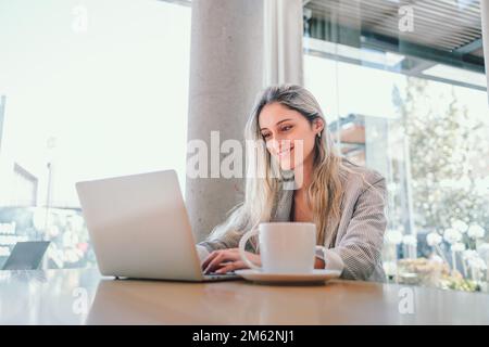 Donna di affari millennial pacifica che usa il laptop, con tazza di caffè in un posto di lavoro moderno. Foto Stock