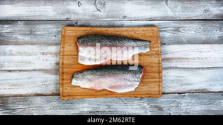 Due filetti, con la pelle rivolta verso l'alto, di salmone alla trota sul tagliere con fondo bianco rustico in legno Foto Stock