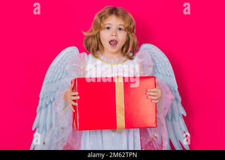 Angelo bambino carino con regalo scatola presente. Angelo di San Valentino. Bambino piccolo cupido. Angelo bambino con ali angeli, isolato su sfondo rosa studio Foto Stock