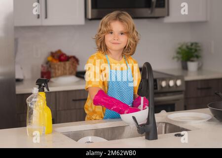 Concetto di lavaggio delle stoviglie. Cute bambino aiutare con la famiglia, detergere piatti in cucina. Adorabile piccolo aiutante servizio di pulizia dei bambini. Piccolo ragazzo carino che scava Foto Stock