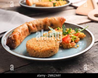 Gustoso Falafel con bulgur piccante e un rotolo di pasta vegetariano su un piatto di ceramica, tradizionale cibo caldo Foto Stock