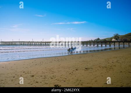 Cayucos, California, USA - Dicembre 25,2022. Ampia spiaggia di sabbia, un vecchio molo di legno e persone che riposano sulla spiaggia. Costa Centrale della California Foto Stock