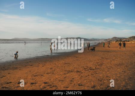 Cayucos, California, USA - 25 dicembre 2022. Ampia spiaggia di sabbia e gente che cammina lungo la riva Foto Stock