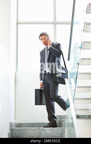 Maturo executive borse da trasporto e parlare sul cellulare. Per tutta la durata di un executive maturo e intelligente che utilizza il telefono cellulare e che cammina lungo la scala con Foto Stock