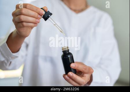 Scienziato femminile in uniforme medica bianca con vetro mock up vaso cosmetico e pipetta in mani Foto Stock