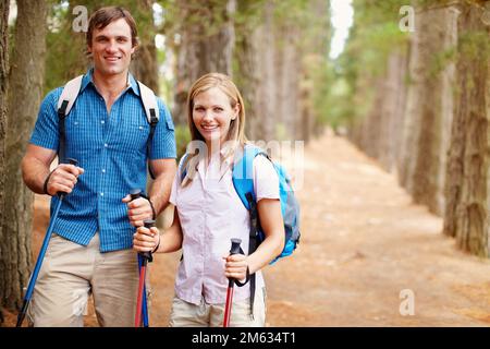 Coppia escursionistica in piedi nel bosco e sorridente. Ritratto di coppia in piedi nel bosco con zaino e pali da trekking e dando un attraente Foto Stock