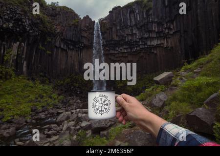 Primo piano mano maschile che imita il riempimento della tazza vicino alla cascata concept photo Foto Stock