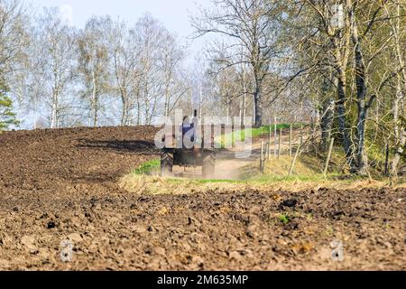 Vecchio trattore che guida su una strada ghiaiata da un campo arato Foto Stock