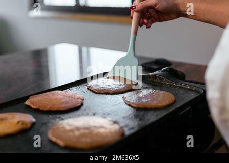 Vista laterale di una donna adulta irriconoscibile e tagliata in piedi al bancone e frittelle con spatola durante la colazione Foto Stock