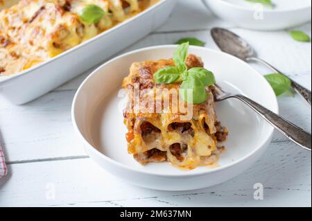 Pezzo di casseruola noodle. Al forno con cannelloni, bolognese e bechamel salsa e mozzarella farcita su sfondo bianco da tavola Foto Stock