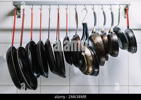 Vaschette in metallo di varie dimensioni appese in fila su ganci attaccati alla ringhiera vicino a una parete piastrellata bianca Foto Stock