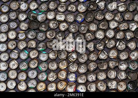 Parete nera decorata con vecchi tappi in metallo delle bottiglie usati sulla strada di giorno come sfondo astratto Foto Stock