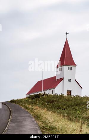 Esterno della chiesa luterana di Reyniskirkja con facciata bianca e tetto rosso contro il cielo sovrastato in Vik i Myrdal in Islanda Foto Stock