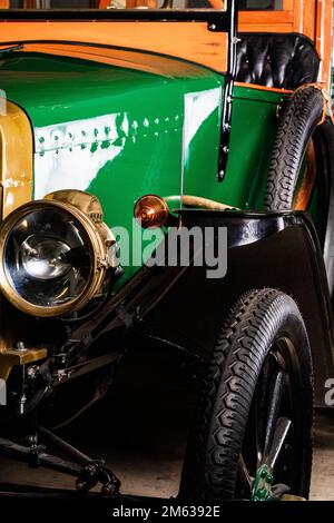 Faro rotondo e grandi ruote di auto da turismo vintage verde e giallo con sedili in pelle nera parcheggiati in garage Foto Stock