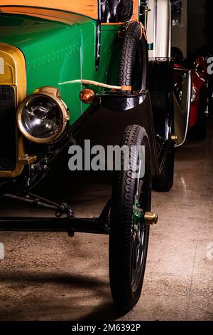 Faro rotondo e grandi ruote di auto da turismo vintage verde e giallo con sedili in pelle nera parcheggiati in garage Foto Stock