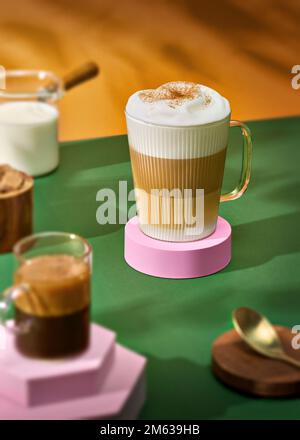 Da sopra la tazza di vetro di latte macchiato fresco posta su un tavolo verde a fuoco selettivo vicino alla tazza di espresso Foto Stock