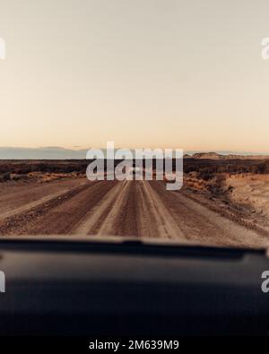 Automobili moderne che guidano su strada asfaltata polverosa vicino al campo asciutto durante il tramonto in Argentina Foto Stock