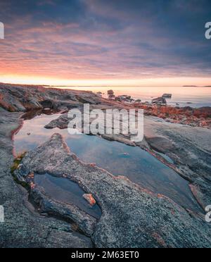 Uno scatto verticale del tramonto luminoso e ipnotico all'orizzonte sopra la costa rocciosa del mare Foto Stock