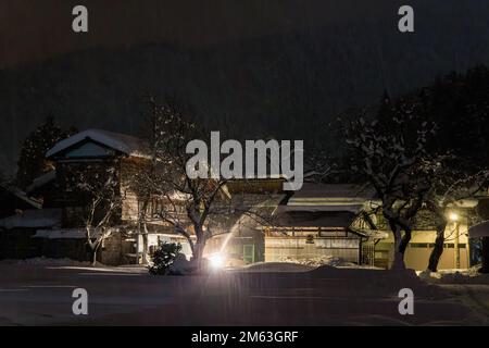 Aratro spara neve durante la tempesta su grande casa giapponese di notte Foto Stock