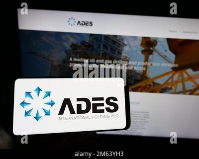 Persona che tiene il cellulare con il logo della società egiziana ADES International Holding sullo schermo di fronte al sito web aziendale. Messa a fuoco sul display del telefono. Foto Stock