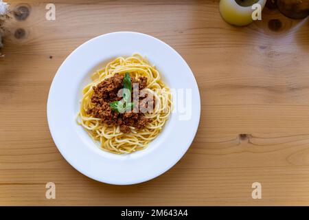 Spaghetti bolognese in piatto bianco, decorato con foglia di basilico su tavolo in legno, Vista dall'alto. Un piatto classico di cucina italiana. Foto Stock
