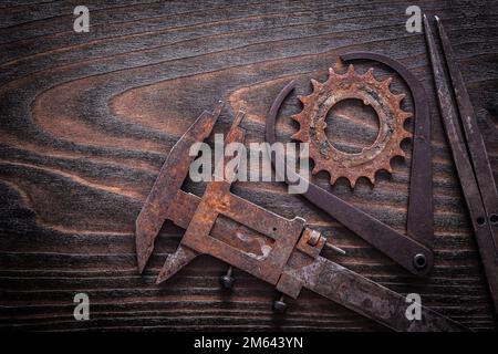 Versione orizzontale di pinze di misura arrugginite con ruota dentata su costruzione di superfici in legno scuro vintage. Foto Stock