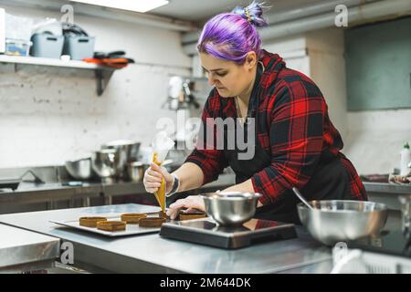Pasticciere femminile che indossa un grembiule per decorare la torta con un sacchetto di pasta con crema. Piccola azienda di cottura. Foto di alta qualità Foto Stock